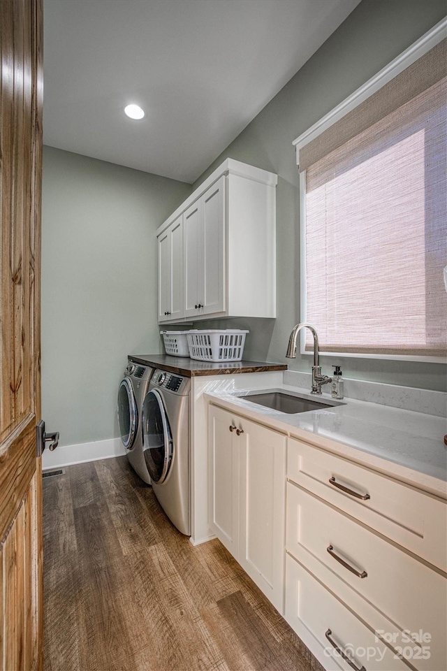 clothes washing area featuring cabinets, sink, washing machine and clothes dryer, and light hardwood / wood-style flooring