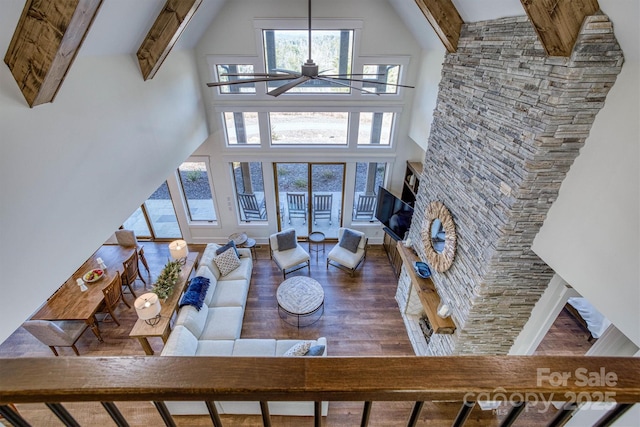 living room with dark hardwood / wood-style floors, a wealth of natural light, a fireplace, a high ceiling, and beam ceiling