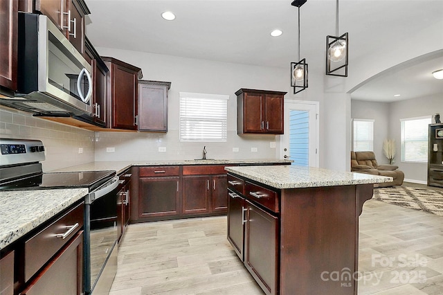 kitchen featuring sink, light stone counters, a kitchen island, pendant lighting, and stainless steel appliances