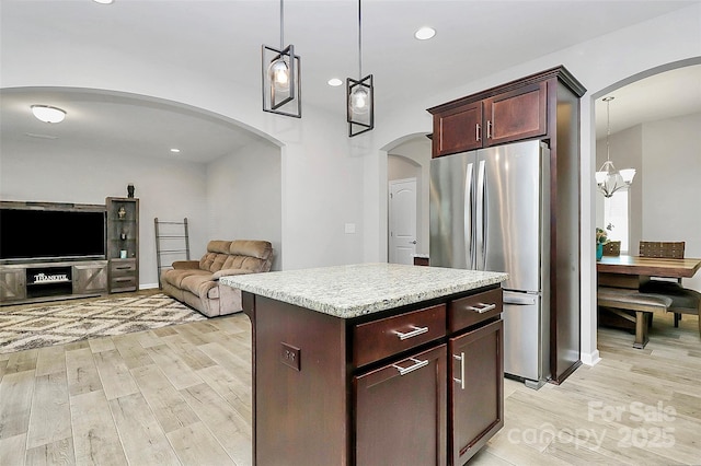 kitchen with hanging light fixtures, a kitchen island, stainless steel fridge, and light hardwood / wood-style floors