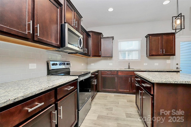 kitchen featuring decorative light fixtures, appliances with stainless steel finishes, light stone countertops, light hardwood / wood-style floors, and backsplash