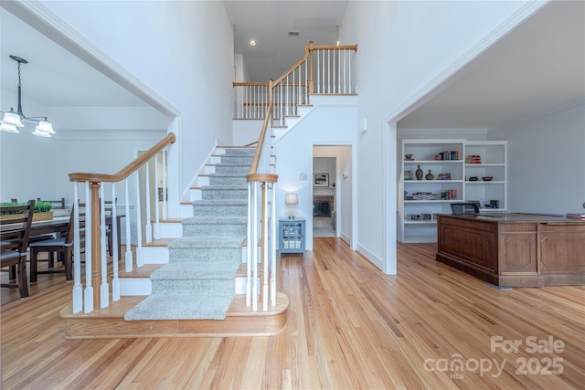 foyer entrance with crown molding, light hardwood / wood-style floors, a high ceiling, and a notable chandelier