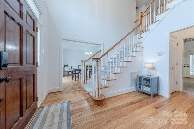 entryway featuring a towering ceiling, a notable chandelier, and light wood-type flooring