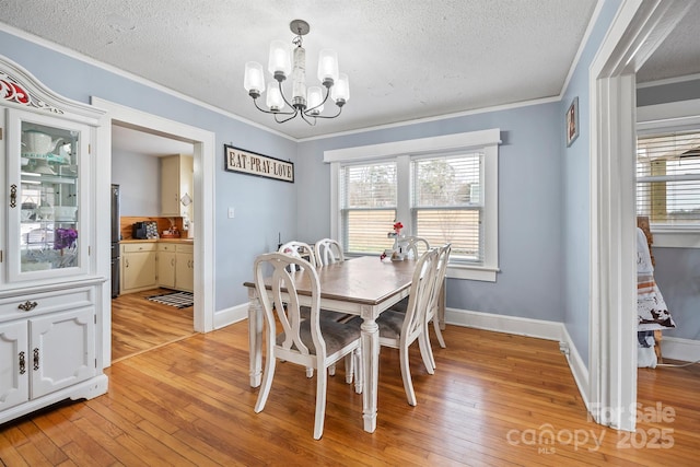 dining area featuring ornamental molding, light wood-type flooring, a textured ceiling, and a chandelier