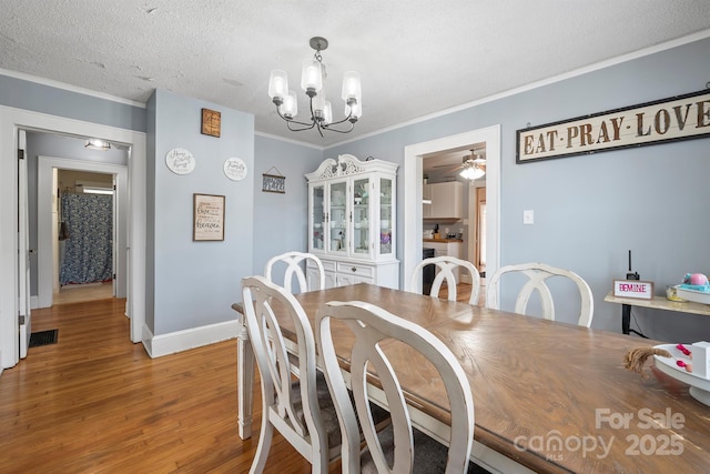 dining space featuring wood-type flooring, ceiling fan with notable chandelier, a textured ceiling, and crown molding