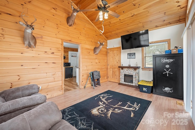 living room featuring a stone fireplace, wood-type flooring, vaulted ceiling, wooden ceiling, and wooden walls