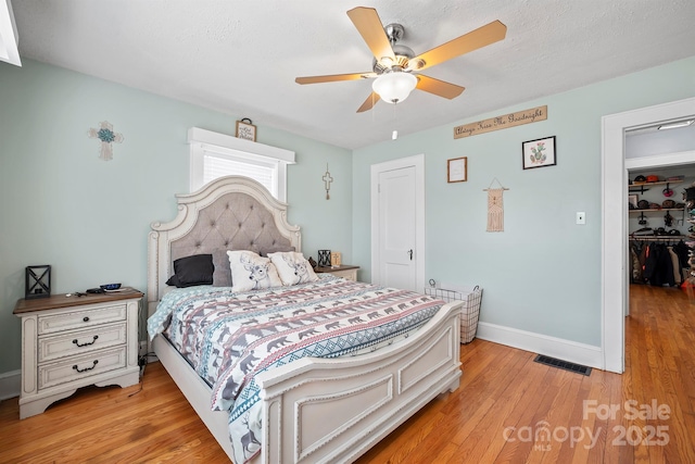 bedroom with light hardwood / wood-style flooring, a walk in closet, ceiling fan, a textured ceiling, and a closet