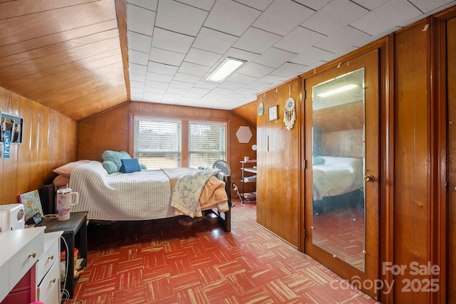 bedroom featuring lofted ceiling, parquet flooring, and wood walls