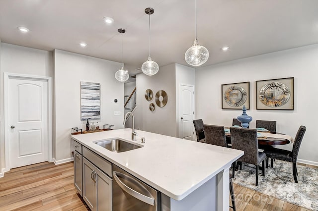 kitchen with sink, a center island with sink, light hardwood / wood-style flooring, dishwasher, and pendant lighting