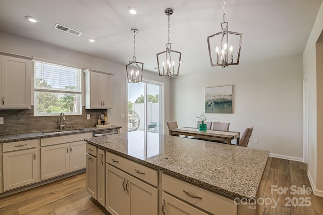 kitchen with light stone counters, decorative light fixtures, sink, and a kitchen island