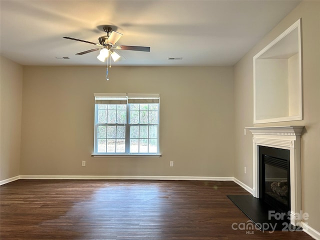 unfurnished living room featuring baseboards, visible vents, dark wood-style flooring, ceiling fan, and a glass covered fireplace