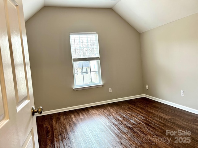 empty room with dark wood finished floors, lofted ceiling, and baseboards