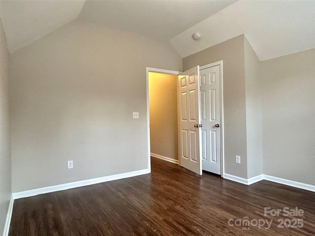 unfurnished bedroom featuring a closet, baseboards, dark wood-type flooring, and lofted ceiling