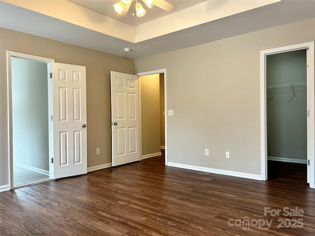 unfurnished bedroom with baseboards, a raised ceiling, a spacious closet, and dark wood-style flooring