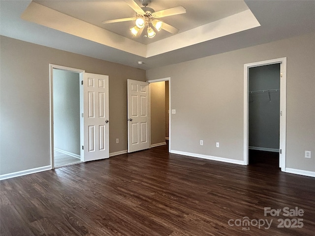 unfurnished bedroom featuring a tray ceiling, baseboards, and dark wood-style flooring