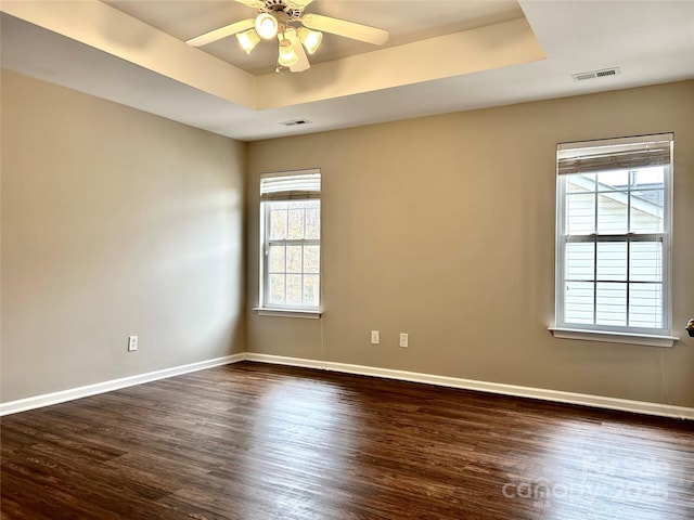 spare room with visible vents, dark wood-type flooring, baseboards, a tray ceiling, and a ceiling fan