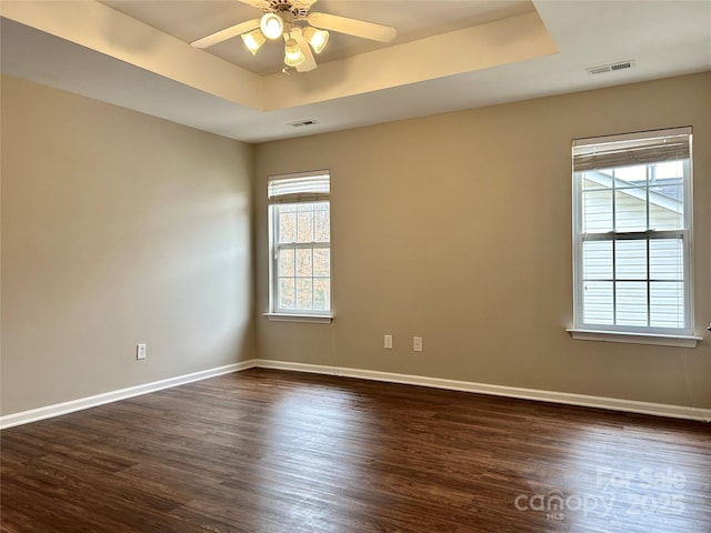 empty room featuring visible vents, dark wood finished floors, baseboards, a raised ceiling, and ceiling fan