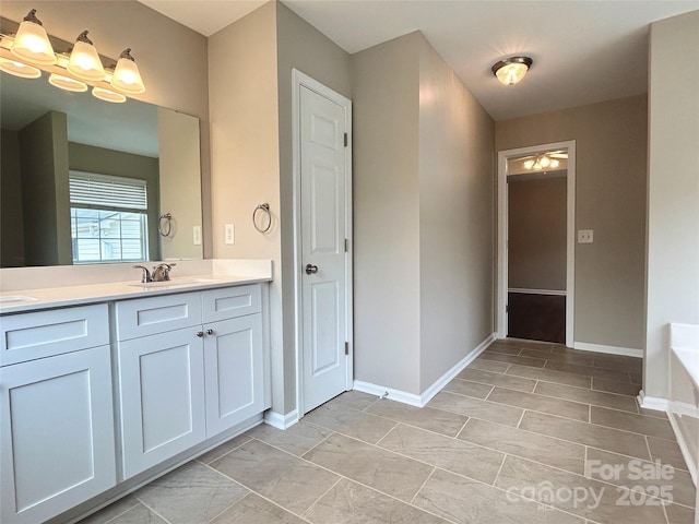 bathroom with baseboards, double vanity, a sink, a bath, and a chandelier