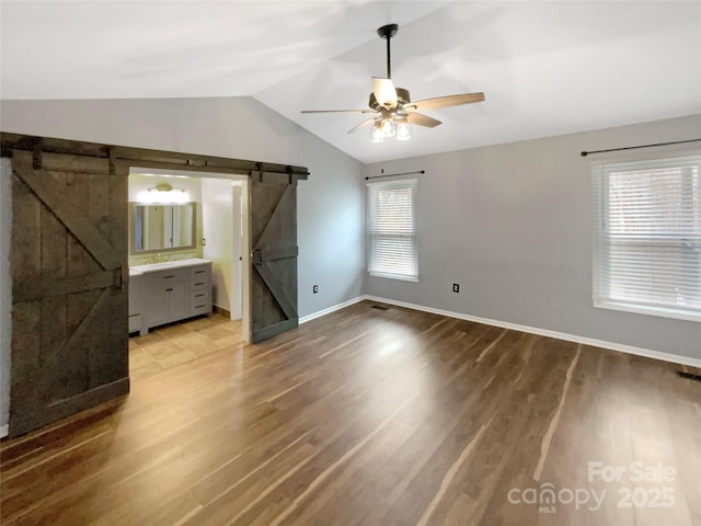 unfurnished bedroom with ceiling fan, lofted ceiling, a barn door, and hardwood / wood-style floors