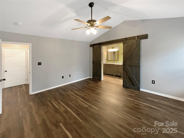 unfurnished bedroom with dark wood-type flooring, ensuite bathroom, vaulted ceiling, ceiling fan, and a barn door