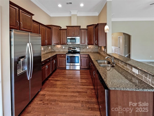 kitchen featuring appliances with stainless steel finishes, dark hardwood / wood-style floors, pendant lighting, sink, and dark stone countertops