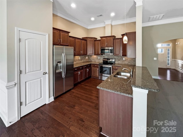 kitchen featuring sink, dark wood-type flooring, dark stone countertops, stainless steel appliances, and kitchen peninsula