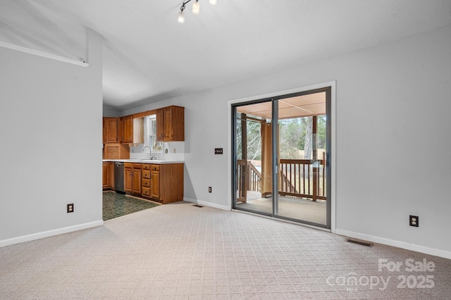 unfurnished living room with vaulted ceiling, sink, light colored carpet, and track lighting