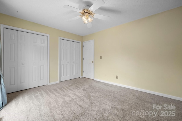 unfurnished bedroom with light carpet, ceiling fan, a textured ceiling, and multiple closets