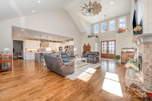 living room featuring high vaulted ceiling, a fireplace, light wood-type flooring, and french doors