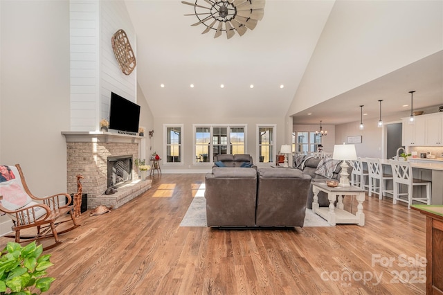 living room featuring a stone fireplace, high vaulted ceiling, a notable chandelier, and light wood-type flooring