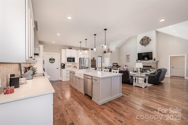 kitchen with hardwood / wood-style flooring, appliances with stainless steel finishes, hanging light fixtures, an island with sink, and white cabinets