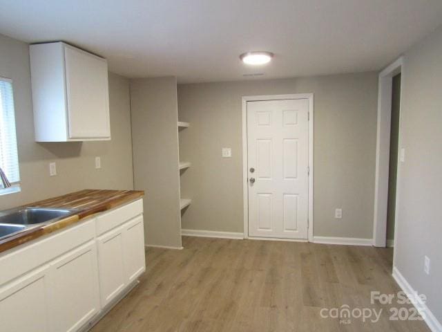 kitchen with sink, white cabinets, wood counters, and light hardwood / wood-style flooring