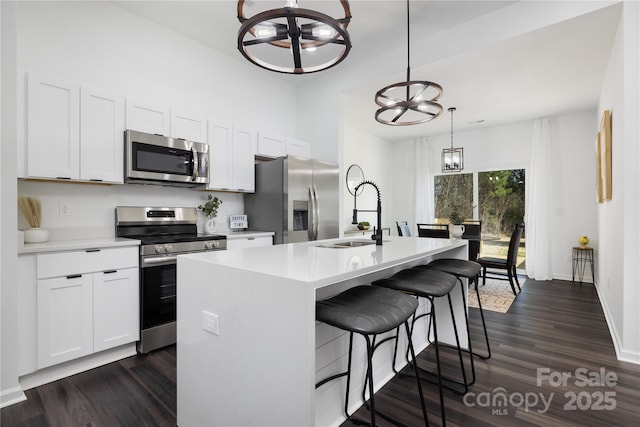 kitchen featuring appliances with stainless steel finishes, decorative light fixtures, sink, a notable chandelier, and a center island with sink