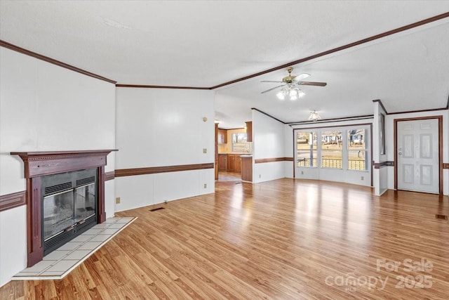 unfurnished living room with lofted ceiling, ceiling fan, ornamental molding, light hardwood / wood-style floors, and a tiled fireplace