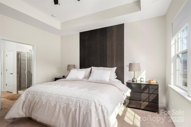 bedroom with a raised ceiling, ceiling fan, and ensuite bath