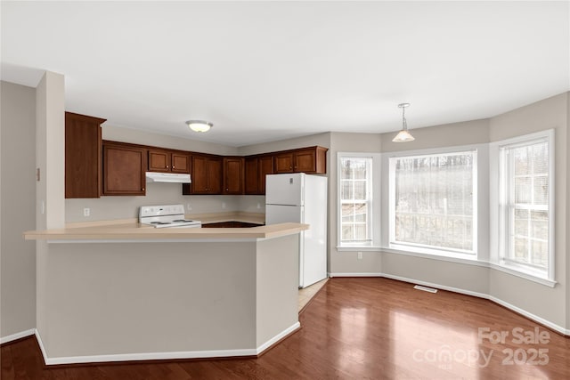 kitchen with white appliances, wood finished floors, a peninsula, light countertops, and under cabinet range hood