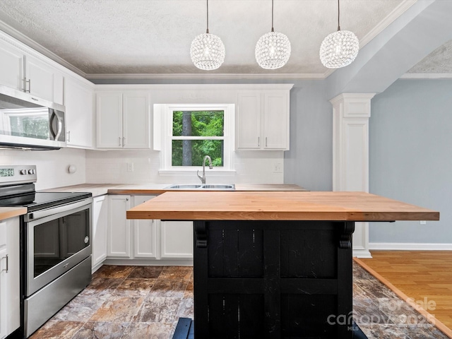 kitchen with sink, appliances with stainless steel finishes, white cabinetry, hanging light fixtures, and wood counters