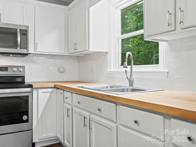 kitchen featuring sink, white cabinetry, stainless steel appliances, wood counters, and decorative backsplash