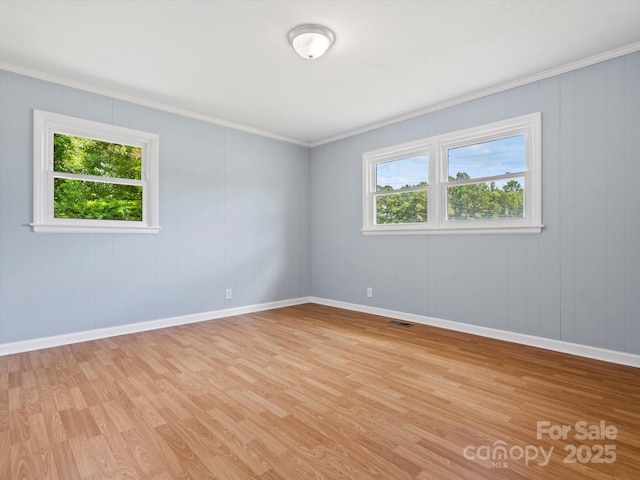 spare room with crown molding, a healthy amount of sunlight, and light wood-type flooring