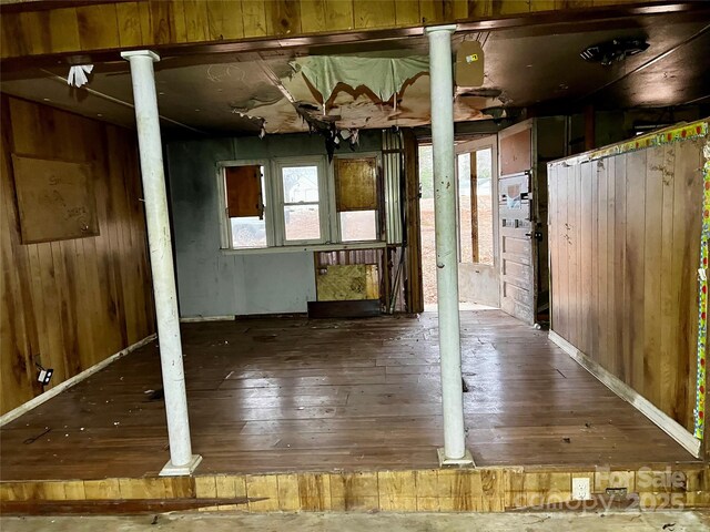 unfurnished room featuring decorative columns, wooden walls, and wood finished floors