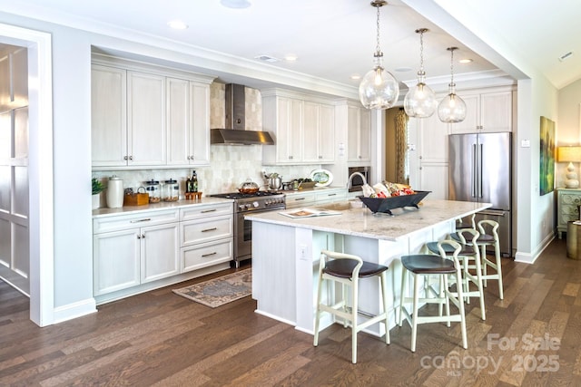 kitchen with a breakfast bar, high quality appliances, a center island with sink, decorative light fixtures, and wall chimney exhaust hood