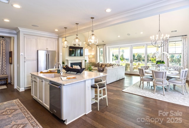 kitchen with pendant lighting, sink, appliances with stainless steel finishes, light stone countertops, and a center island with sink