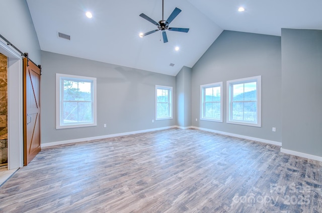 interior space featuring ceiling fan, a barn door, high vaulted ceiling, and light wood-type flooring