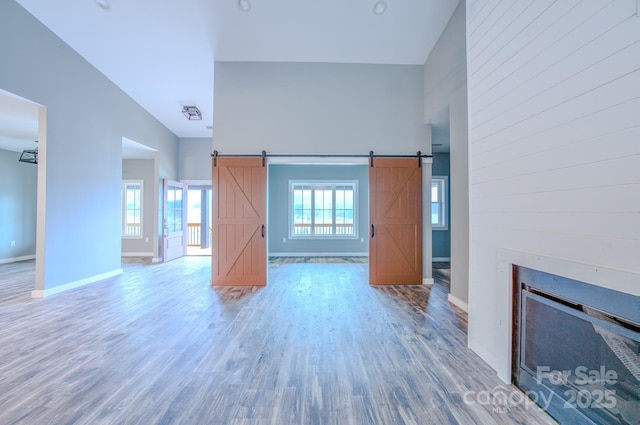 unfurnished living room featuring hardwood / wood-style floors, high vaulted ceiling, and a barn door