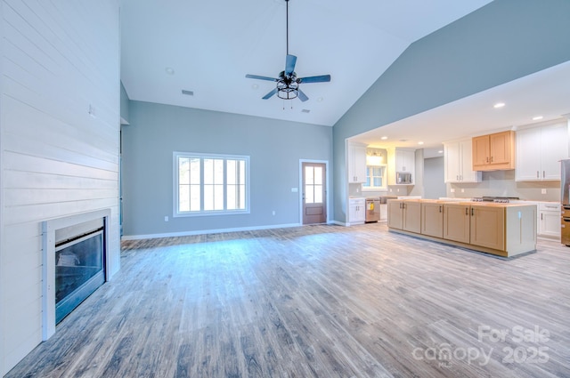 unfurnished living room with ceiling fan, high vaulted ceiling, a large fireplace, and light wood-type flooring