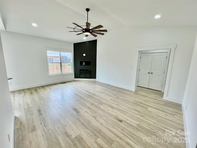 unfurnished living room featuring vaulted ceiling, light hardwood / wood-style floors, a large fireplace, and ceiling fan