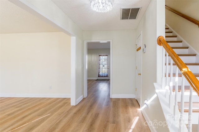 hall featuring an inviting chandelier, a textured ceiling, and light hardwood / wood-style flooring