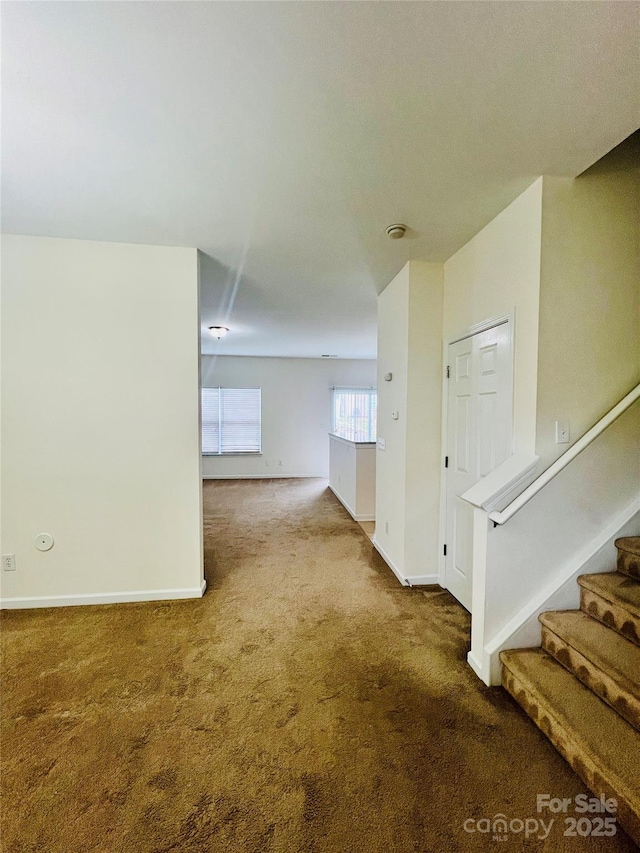 carpeted empty room featuring stairway and baseboards