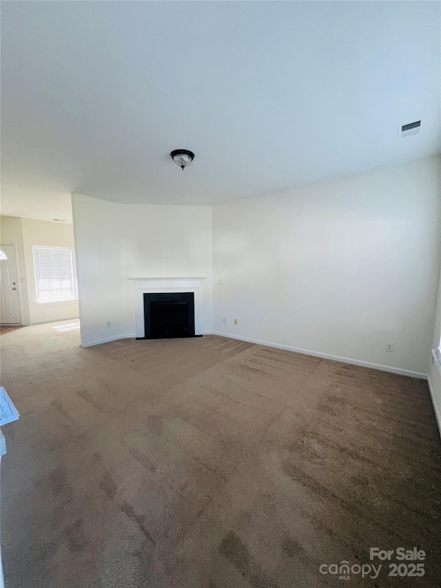 unfurnished living room featuring a fireplace with flush hearth, baseboards, visible vents, and carpet flooring