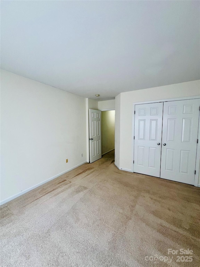 unfurnished bedroom featuring light carpet, a closet, and baseboards